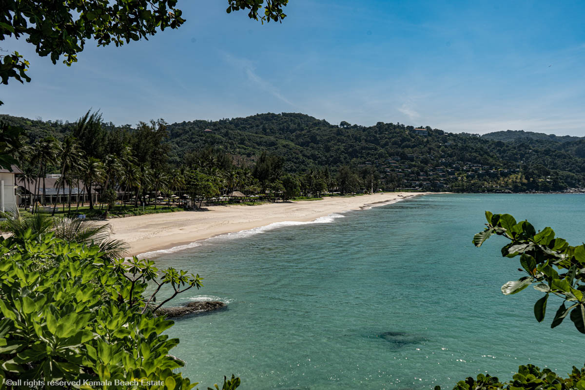 Beachgoers at Kata Noi Beach in Phuket, with soft white sand, turquoise waters, and lush greenery in the background.