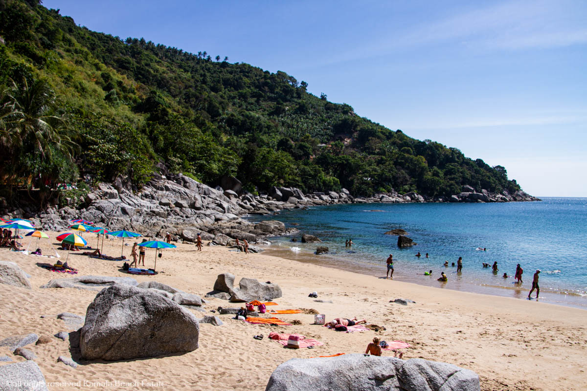 Beachgoers at Nui Beach in Phuket, with soft white sand, turquoise waters, and lush greenery in the background.