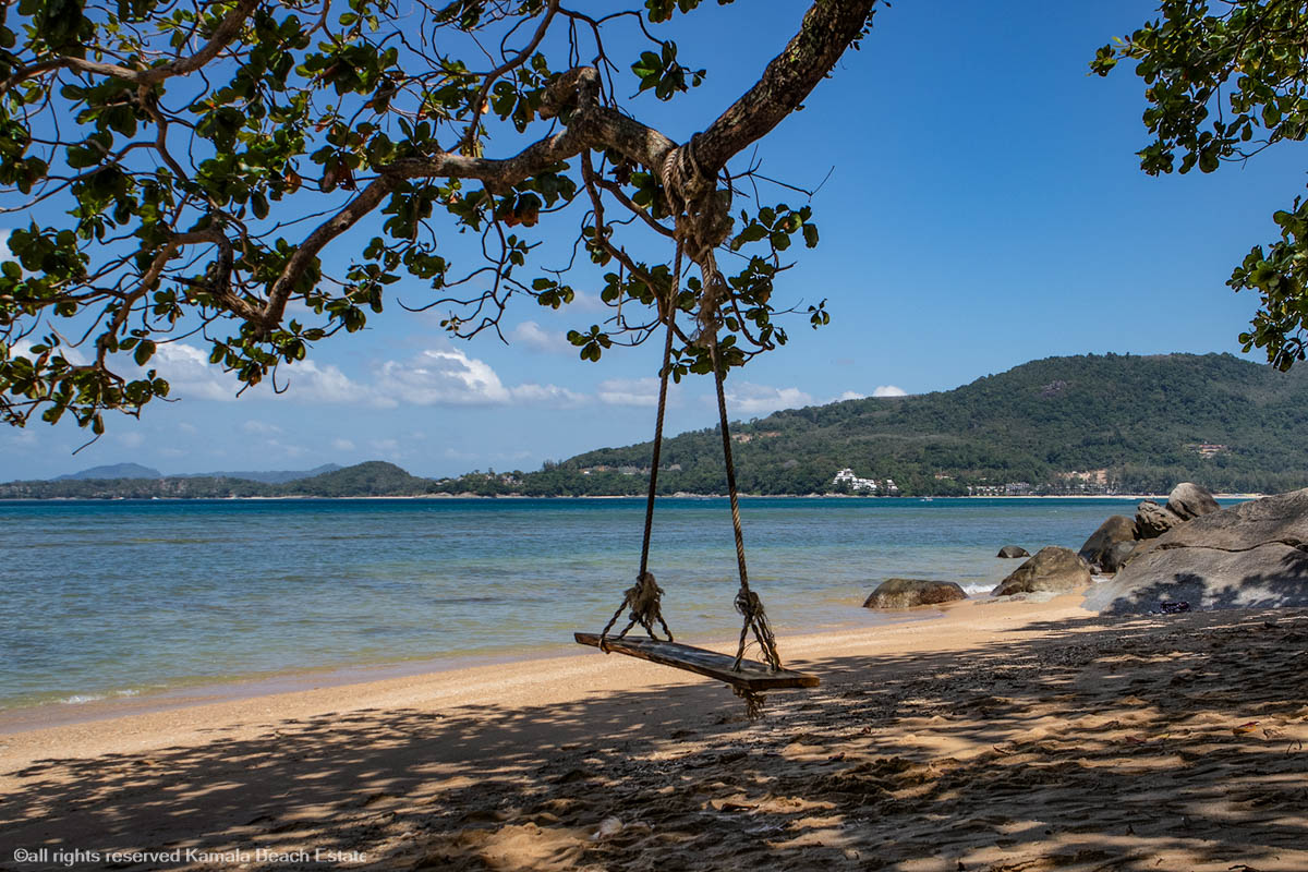 Tranquil view of Rayee Beach with clear blue waters and a rocky shoreline.