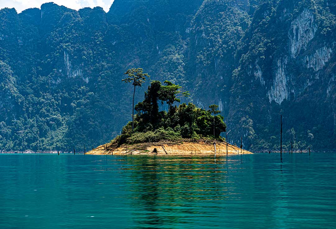 Khao Sok National Park - Small lush green island on Cheow Lan Lake with towering limestone cliffs in the background.