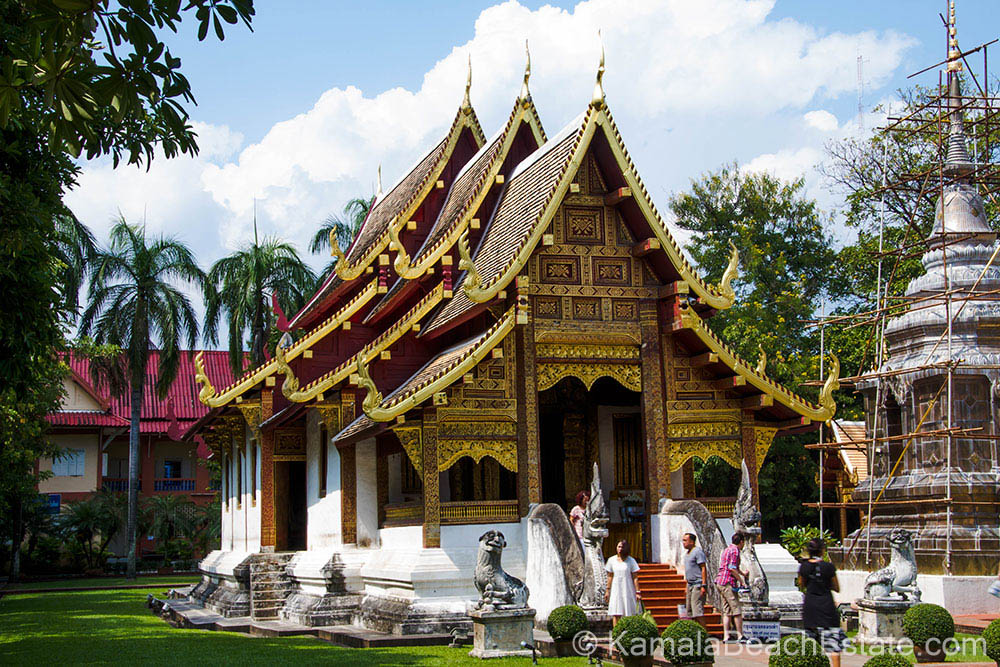 Exterior view of Wat Phra Sing Temple in Chiang Mai, showcasing traditional Lanna architecture with golden carvings and red-roofed structures, surrounded by greenery and visitors