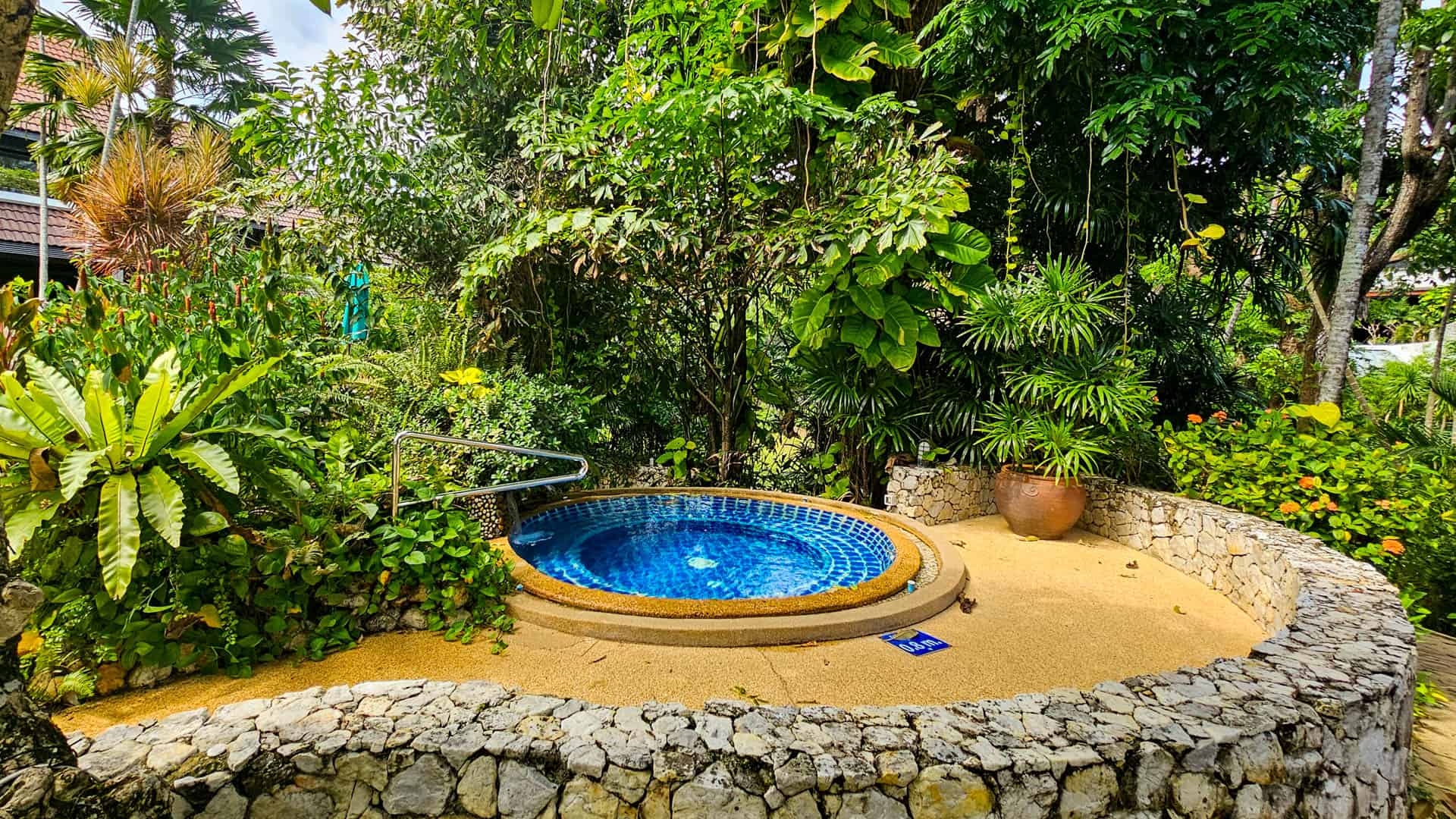 The circular jacuzzi surrounded by tropical plants and a low stone wall